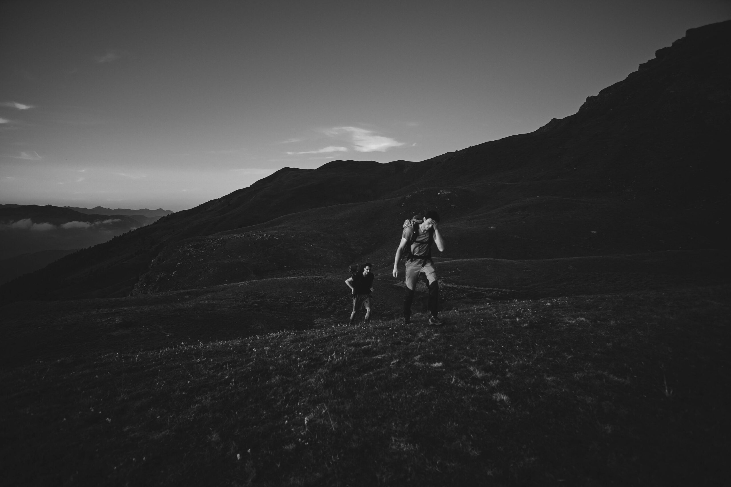 Two hikers trekking through mountainous terrain in dramatic black and white, Cesana Torinese.